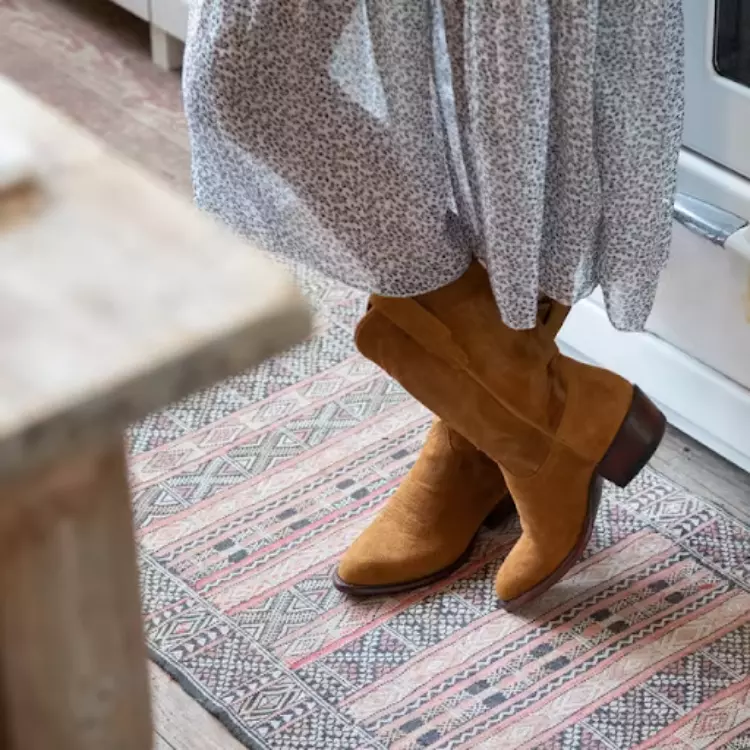 Woman crossing ankles wearing suede boots while standing in a kitchen