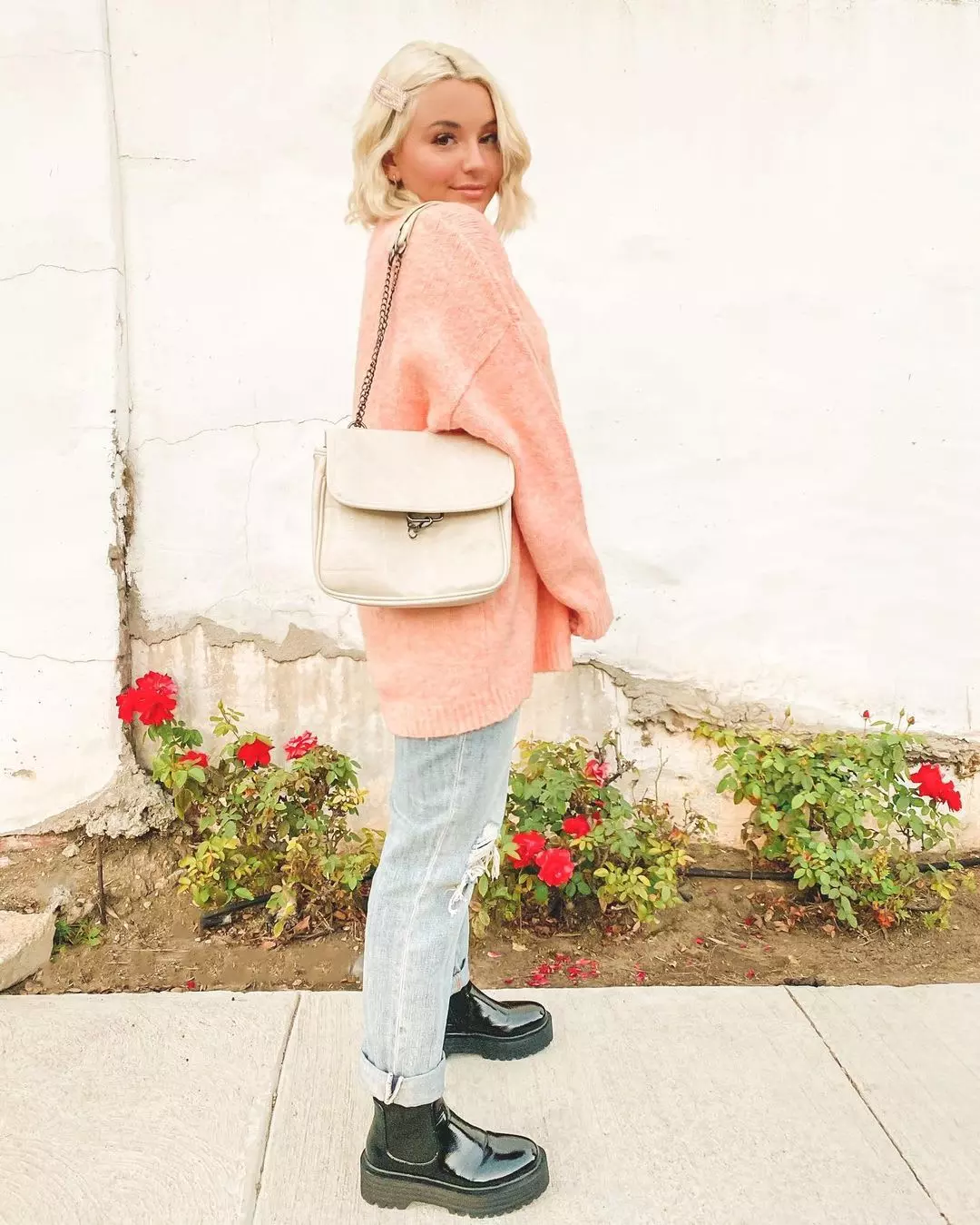 Woman wearing an oversized pink sweater with cuffed distressed jeans and patent boots