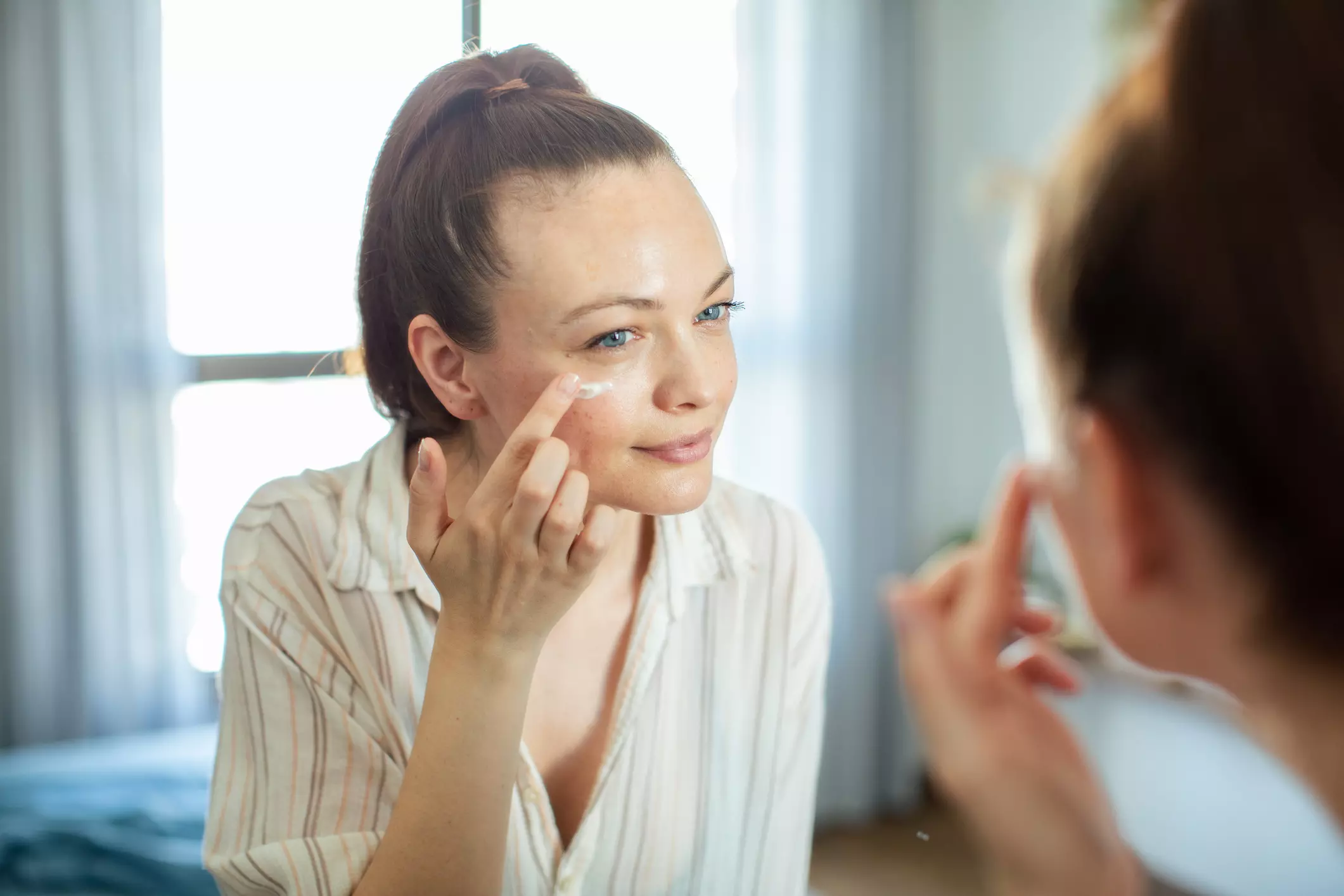 Woman putting moisturizer on in the mirror.