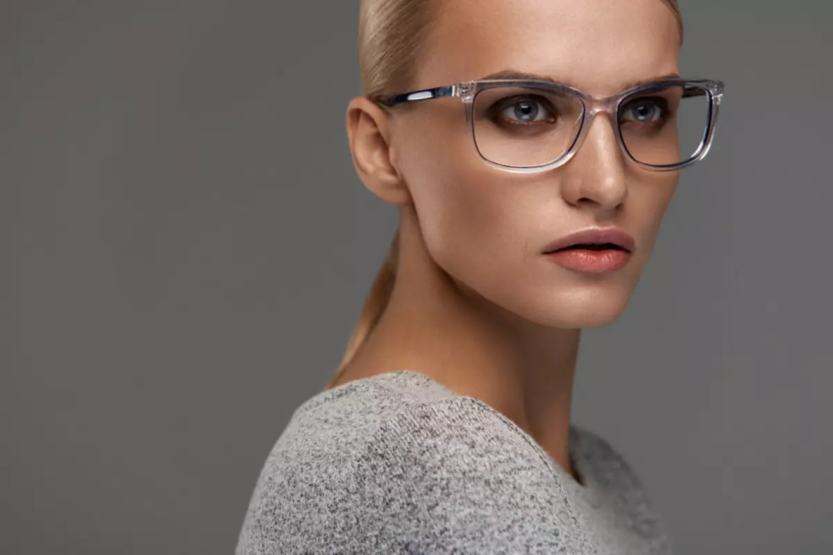 Female Eyewear. Attractive Blonde Girl With Natural Face Makeup In Transparent Glasses Frame. Beautiful Young Woman Wearing Stylish Fashion Optical Eye Glasses On Grey Background. High Resolution